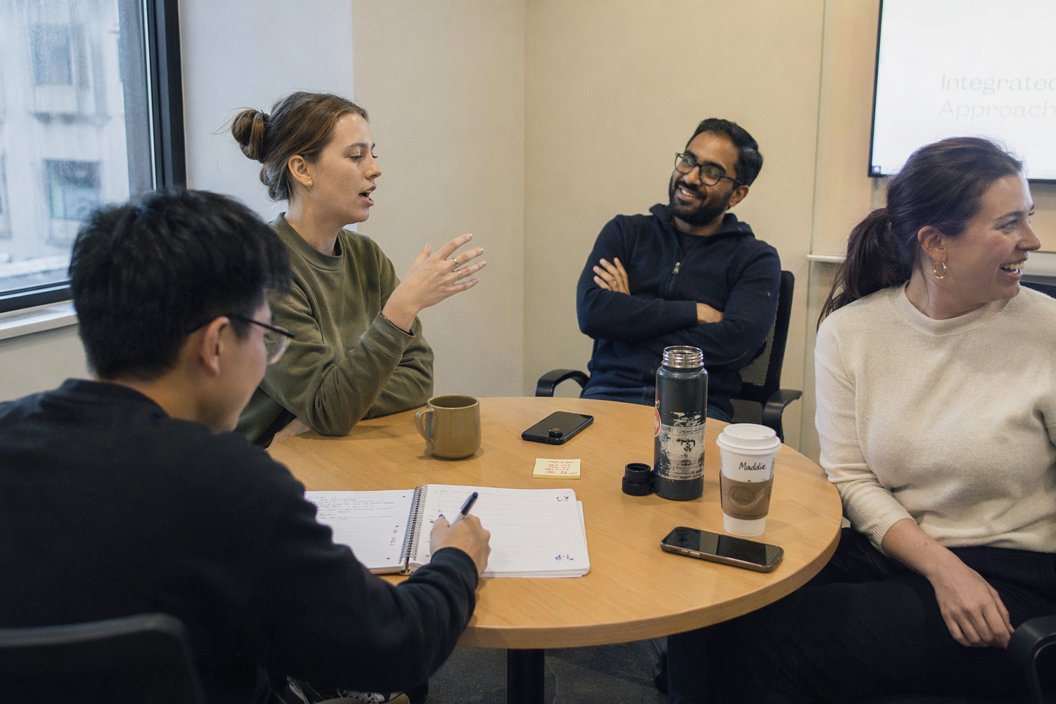 A team of coworkers gathered around a table in a bright office, laughing and engaged in conversation